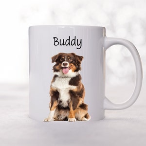May include: White ceramic mug with a brown and white Australian Shepherd dog sitting on it. The dog is looking at the camera and has its tongue sticking out. The text "Buddy" is printed on the mug.