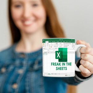 K&ouml;nnte beinhalten: Eine wei&szlig;e Kaffeetasse mit einem gr&uuml;nen und wei&szlig;en Microsoft Excel-Tabellenblatt-Design. Der Text "Freak in the Sheets" ist auf die Tasse gedruckt.