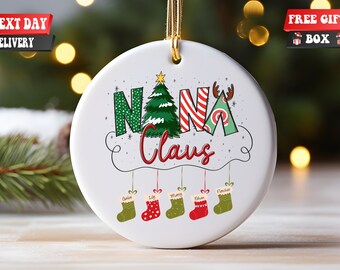 May include: White ceramic Christmas ornament with the text "NANA CLAUS" in colorful letters. A green Christmas tree is incorporated into the "N" and a red and white striped pattern is incorporated into the "A". Five stockings hang below with the names "Caleb", "Lily", "Manny", "Ethan", and "Fincher" written on them.