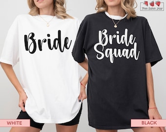 Puede incluir: Dos camisetas de gran tamaño, una blanca y otra negra. La camiseta blanca tiene la palabra "Bride" en escritura negra. La camiseta negra tiene las palabras "Bride Squad" en escritura blanca. Ambas camisetas son parte de una colección nupcial.