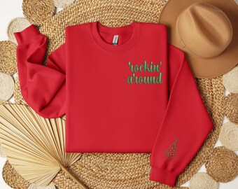 May include: A red sweatshirt with the text "rockin' around" in green on the chest and a green Christmas tree design on the sleeve. The sweatshirt is made of a soft material and is perfect for the holiday season.