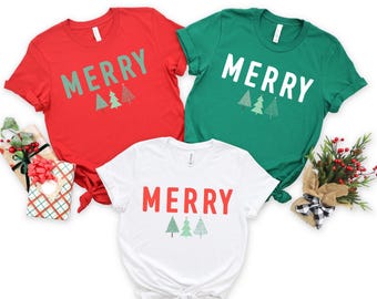 May include: Three t-shirts with the word "Merry" and a design of three stylized Christmas trees. The shirts are red, green, and white.
