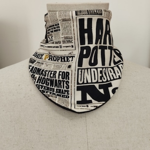 Può includere: Un passamontagna in tessuto bianco con una stampa nera di un titolo di giornale che recita "Harry Potter e i No Indesiderabili" e "Preside di Hogwarts Severus Piton Confermato".