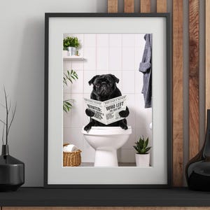 May include: Framed print of a black pug on a toilet, reading a newspaper. The newspaper is titled "The Daily Scoop" with headlines "Wanted" and "Who Left The Seat Up?" The bathroom setting includes plants and a towel.
