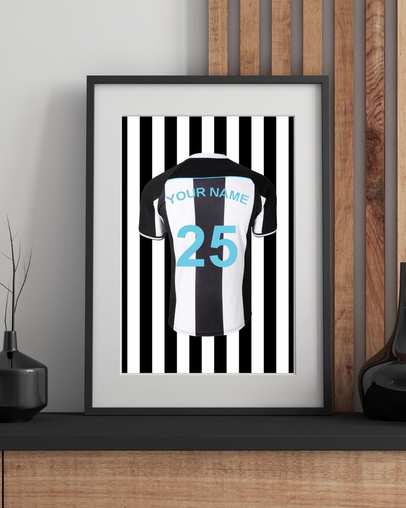 Peut inclure: Impression encadr&eacute;e d'un maillot de football &agrave; rayures noires et blanches avec le num&eacute;ro 25 en bleu clair. Le maillot a un col et des manches noirs, et les mots "YOUR NAME" sont au-dessus du num&eacute;ro. Le fond est &agrave; rayures verticales noires et blanches.