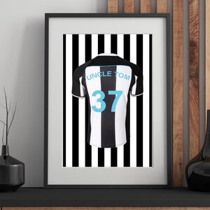 Peut inclure: Impression encadr&eacute;e d'un maillot de football &agrave; rayures noires et blanches avec le nom "UNCLE TOM" et le num&eacute;ro "37" en bleu clair. Le maillot est centr&eacute; sur un fond &agrave; rayures noires et blanches.