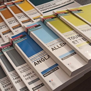 Peut inclure: Une pile de livres scolaires jaunes, bleus et gris avec le mot "CNED" imprimé sur les dos. Le texte sur les couvertures comprend des titres tels que "Tourisme et Territoire", "Anglais" et "Allemand".