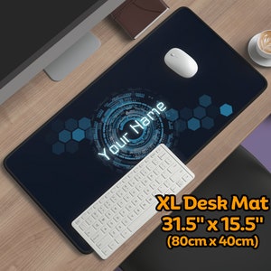 Op de afbeelding: Een grote zwarte bureau mat met een blauw en wit geometrisch ontwerp. De mat heeft de tekst "Your Name" in een wit lettertype. De mat meet 80 cm x 40 cm.