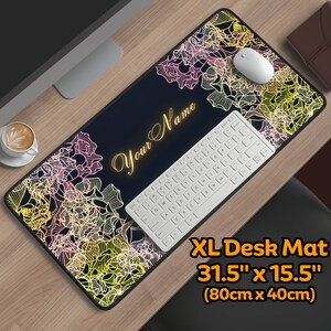 Op de afbeelding: Een zwarte bureau mat met een bloemenpatroon in roze, geel en wit. De mat is 80 cm bij 40 cm. De tekst "Your Name" is in goud op de mat geschreven.