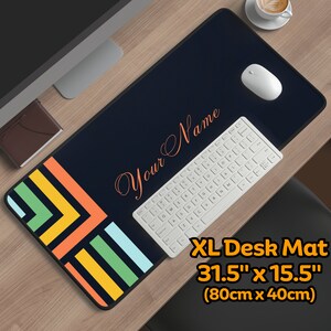 Könnte beinhalten: Eine schwarze und blaue Schreibtischunterlage mit einem geometrischen Muster in Orange, Gelb und Grün. Die Unterlage ist 80 cm x 40 cm groß und trägt den Text "Your Name" in einer kursivschrift.