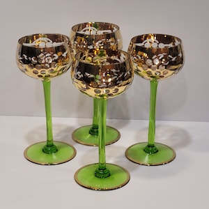 May include: Set of four green glass stemmed wine glasses with gold and white etched designs. The glasses have a gold rim and a green stem.