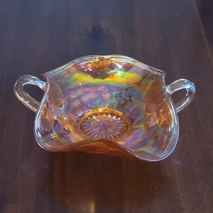 May include: A vintage iridescent orange glass bowl with two handles. The bowl has a scalloped edge and a textured design.