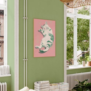 May include: A pink framed print of a white and green cat with its eyes closed, lying on its back with its paws in the air. The cat is on a pink background.