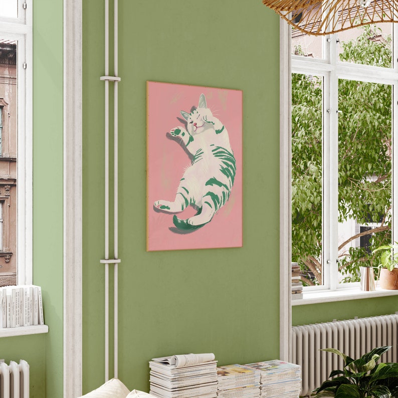 May include: A pink framed print of a white and green cat with its eyes closed, lying on its back with its paws in the air. The cat is on a pink background.