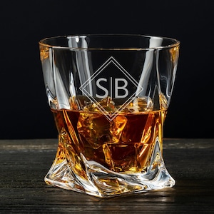 May include: A clear glass rocks glass with a twisted design and the initials "SB" etched on the front. The glass is filled with amber-colored liquid and ice cubes.