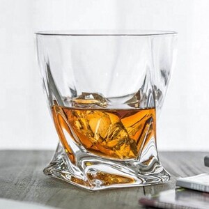May include: A clear glass whiskey tumbler with a unique, twisted design. The glass is filled with amber-colored whiskey and ice cubes.
