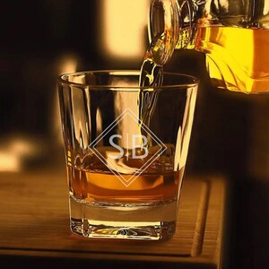 May include: A clear glass rocks glass with a gold liquid being poured into it. The glass has the initials "S|B" etched on the side.