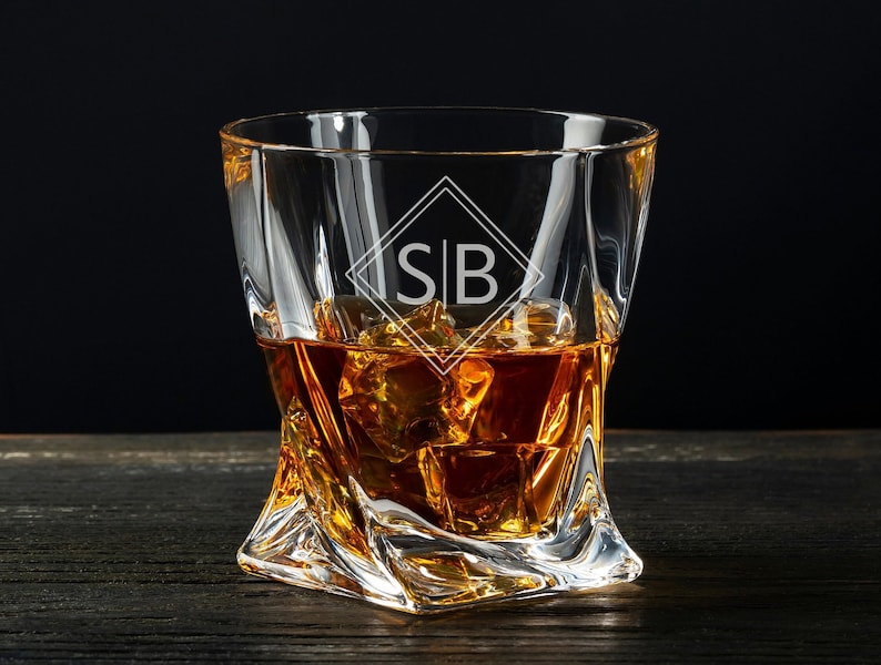 May include: A clear glass rocks glass with a twisted design and the initials "SB" etched on the front. The glass is filled with amber-colored liquid and ice cubes.
