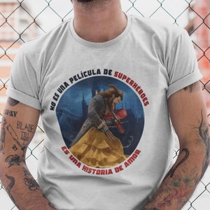 Op de afbeelding: Een wit T-shirt met een ronde afbeelding waarop een cartoon van het Beest uit Belle en het Beest te zien is terwijl hij met Belle danst. De afbeelding bevat Spaanse tekst die luidt "No es una pel&iacute;cula de superh&eacute;roes. Es una historia de amor."