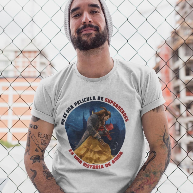 Op de afbeelding: Een wit T-shirt met een ronde afbeelding waarop een cartoon van het Beest uit Belle en het Beest te zien is terwijl hij met Belle danst. De afbeelding bevat Spaanse tekst die luidt "No es una pel&iacute;cula de superh&eacute;roes. Es una historia de amor."