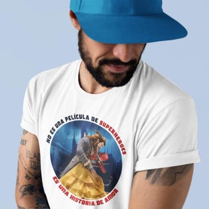 Op de afbeelding: Een wit T-shirt met een ronde afbeelding van een sc&egrave;ne uit de film Belle en het Beest. De afbeelding bevat Spaanse tekst die luidt "No es una pel&iacute;cula de superh&eacute;roes. Es una historia de amor."