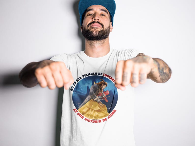 Op de afbeelding: Wit T-shirt met een ronde afbeelding van een man en een vrouw in een kasteelomgeving. De tekst rond de afbeelding luidt "No es una pelicula de superheroes, es una historia de amor."