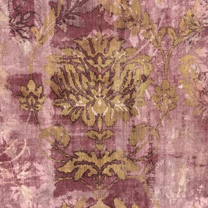 May include: A close-up of a patterned fabric with a damask design. The fabric features a distressed look with a color palette of burgundy, gold, and pale pink. The design includes floral and leaf motifs.