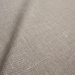 May include: Close-up of a textured, neutral-toned fabric. The material has a woven appearance with a subtle pattern, creating a soft, tactile look. The colour is a muted beige or light brown.