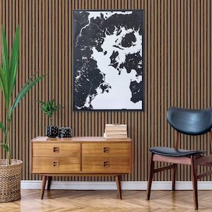 May include: A mid-century modern style wooden dresser with four drawers, a black and white map print hanging on the wall above it, a potted plant on the left, and a black leather chair on the right. The wall is covered in brown wood paneling.