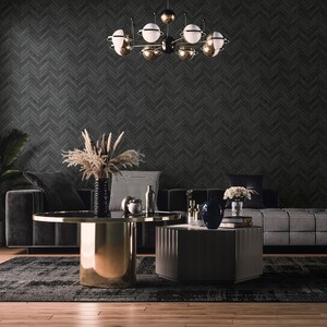 May include: A black and white checkered sofa with black throw pillows sits in front of a dark gray herringbone patterned wall. A gold metal coffee table with a glass top sits in front of the sofa. A smaller, hexagonal coffee table with a dark wood top sits in front of the larger table. A vase with dried flowers sits on the larger table.