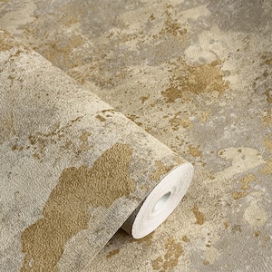 May include: A roll of wallpaper featuring a textured surface with an abstract pattern of metallic gold and muted gray tones. The design consists of irregular, splattered shapes that create a layered effect across the entire material surface.