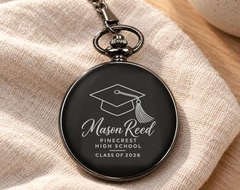 Könnte beinhalten: Eine schwarze Taschenuhr mit silberner Kette, graviert mit einem Doktorhut-Symbol und dem Text Mason Reed, Pinecrest High School, Class of 2026. Die Uhr hat ein kreisförmiges Zifferblatt mit glatter Oberfläche und eine metallische Krone.