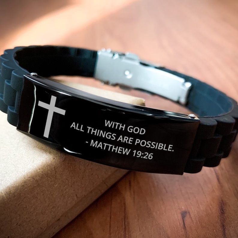 May include: Black silicone bracelet with a silver metal clasp and a black metal plate with the words "With God all things are possible. - Matthew 19:26" and a silver cross.