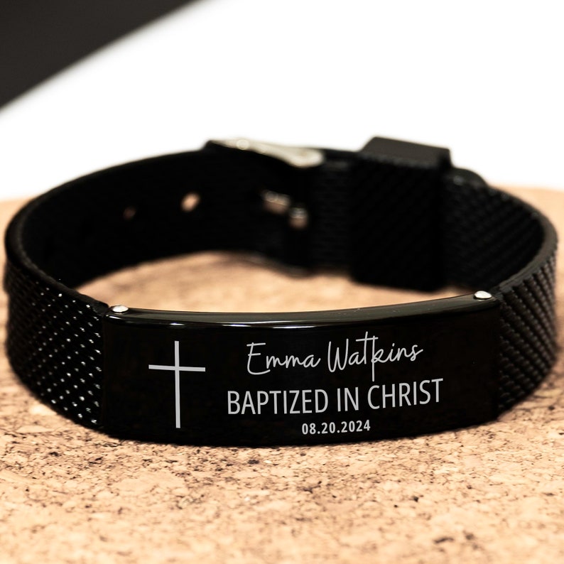 K&ouml;nnte beinhalten: Schwarzes Armband mit einer silbernen Metallplatte, die mit einem Kreuz, dem Namen "Emma Watkins", dem Text "Getauft in Christus" und dem Datum "08.20.2024" graviert ist.