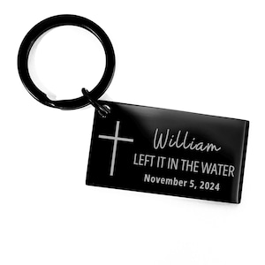 May include: Black metal keychain with a cross and the inscription "William LEFT IT IN THE WATER November 5, 2024".