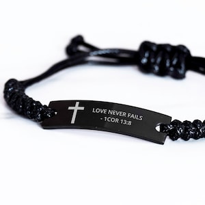 May include: Black braided bracelet with a black metal tag that reads "LOVE NEVER FAILS - 1 COR 13:8" and features a silver cross.