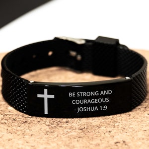May include: Black silicone bracelet with a silver metal plate engraved with a cross and the words "Be strong and courageous - Joshua 1:9".