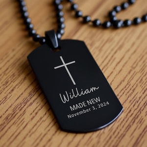 May include: Black dog tag necklace with a silver cross and the inscription "William MADE NEW November 3, 2024".