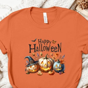 May include: Orange t-shirt with a graphic of three pumpkins with faces and a witch's hat. The text "Happy Halloween" is above the pumpkins.