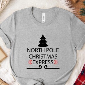 May include: Grey t-shirt with a black Christmas tree and the text "North Pole Christmas *Express*" with red snowflakes.