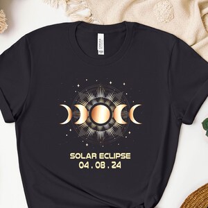 May include: Black t-shirt with a gold graphic of a solar eclipse with the text "SOLAR ECLIPSE 04.08.24"
