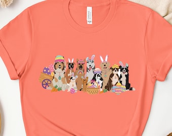 May include: A coral pink t-shirt with a graphic of a group of dogs wearing bunny ears and holding Easter eggs. The dogs are all different breeds and sizes.