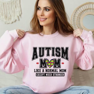 a woman sitting on a bed wearing a pink sweatshirt