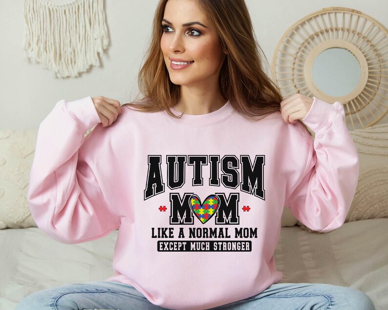 a woman sitting on a bed wearing a pink sweatshirt