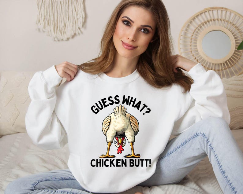 a woman sitting on a bed wearing a white shirt with a chicken saying guess what