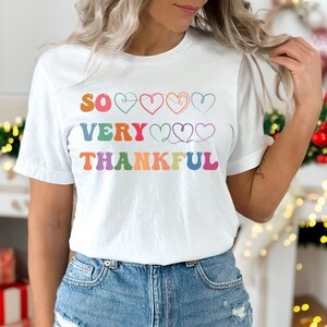 May include: White t-shirt with the text "SO VERY THANKFUL" in rainbow colors with hearts between the words.