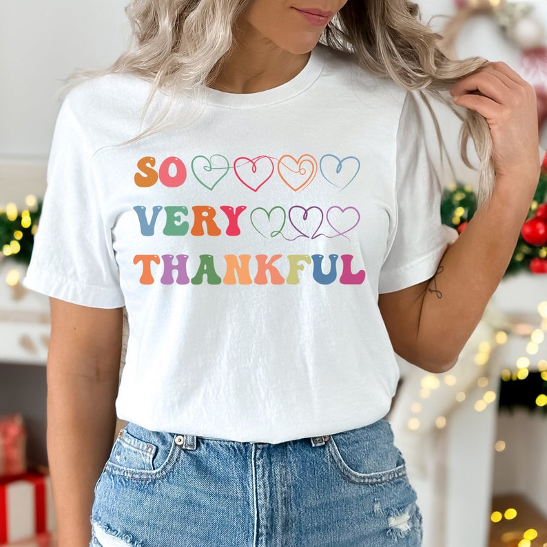 May include: White t-shirt with the text "SO VERY THANKFUL" in rainbow colors with hearts between the words.