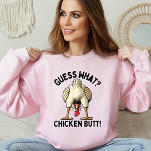 a woman sitting on a bed wearing a pink sweatshirt