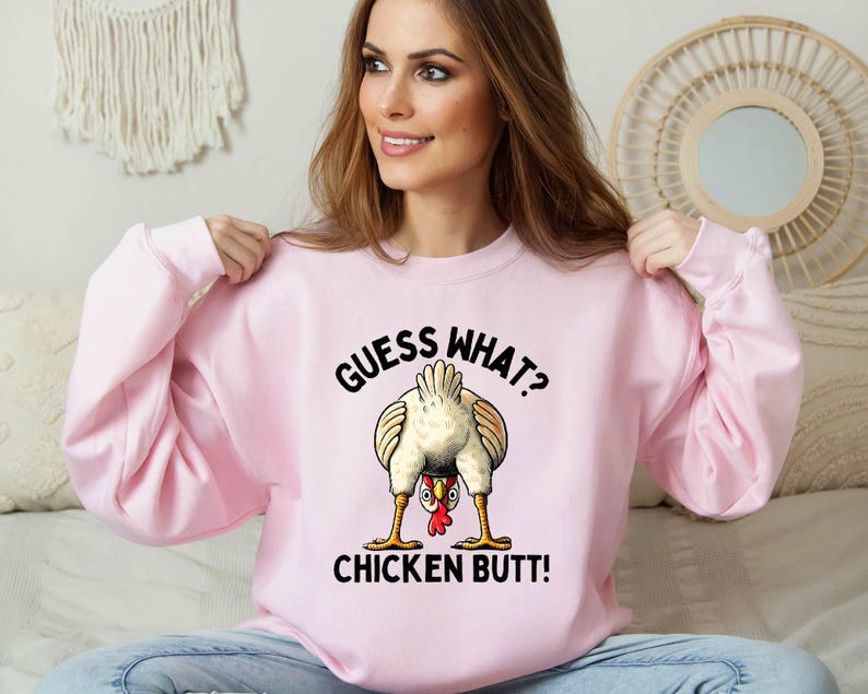 a woman sitting on a bed wearing a pink sweatshirt
