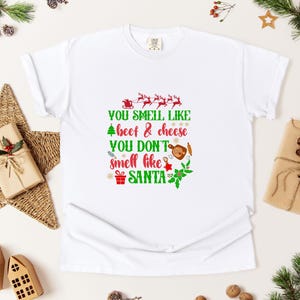 May include: White t-shirt with a Christmas-themed graphic that says "You smell like beef & cheese You don't smell like Santa".